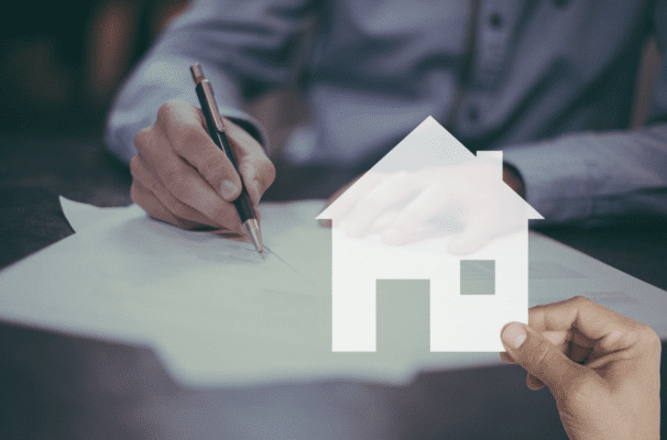 A person writing on some paper. A hand holding a white icon of a home is laid over the image