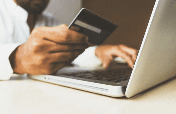 Person completing a purchase online using a laptop and holding a credit card