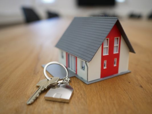 Photo of a small model house on a table next to a key on a keychain