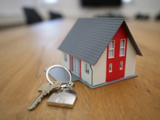 Photo of a small model house on a table next to a key on a keychain