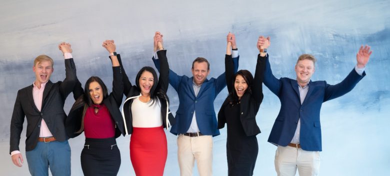 Group photo of the Home Tax Solutions Originations Team and CEO Trey Rome grasping hands with their arms up in a celebratory manner